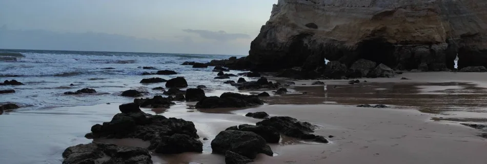 a view of the beach at sunset with rocks on the shore