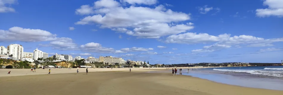 a sandy beach with people walking on it and buildings in the background